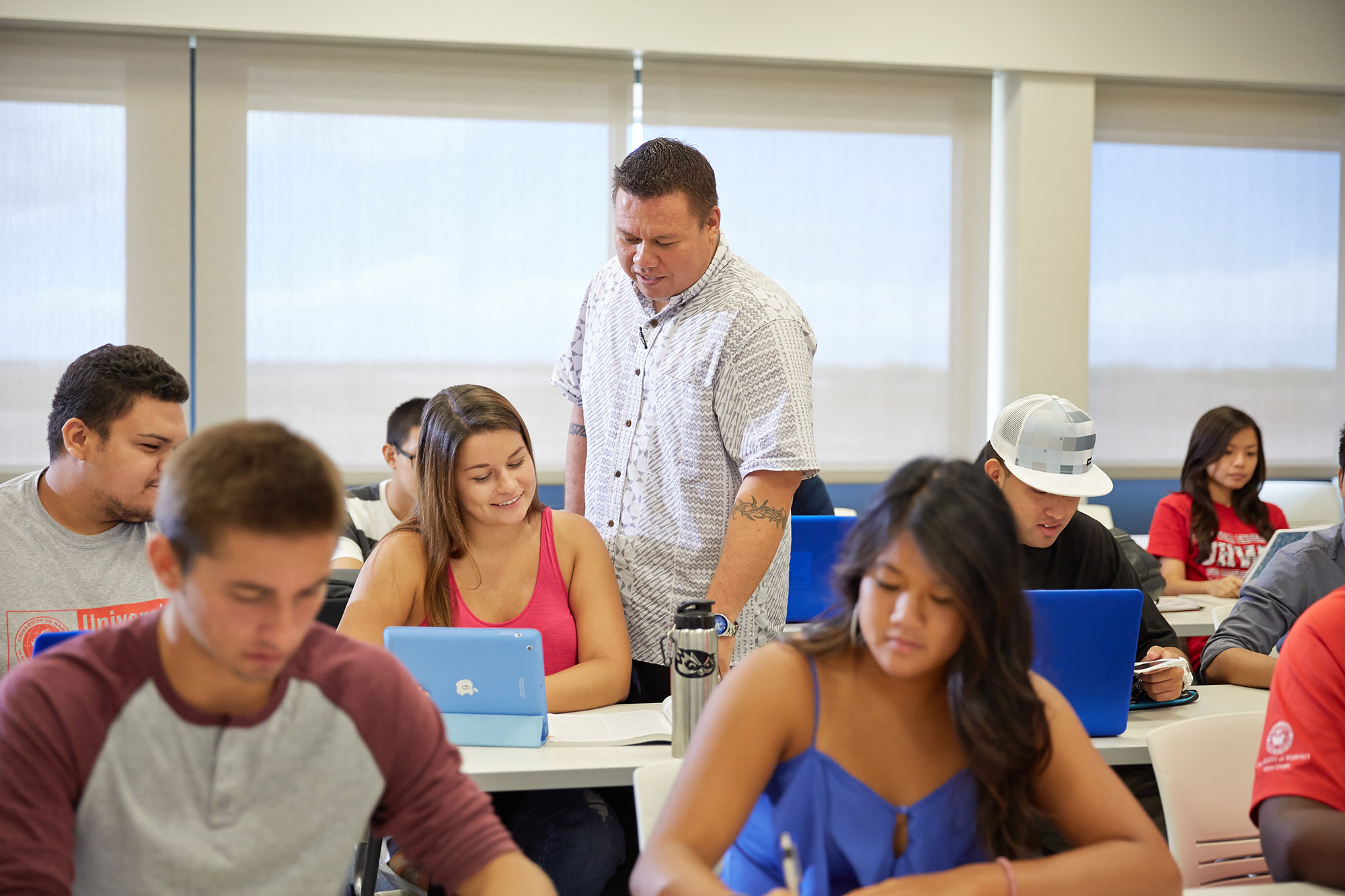 Professor standing in the middle of classroom, looking over student's shoulder.