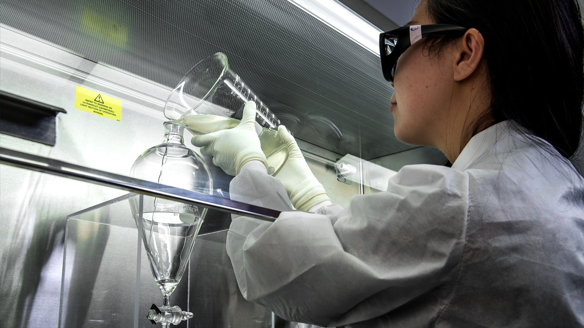 Someone working in a laboratory setting pouring liquid into a beaker.