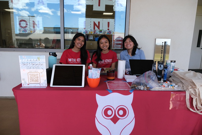 Three women who work at the Noeau Center sitting at a table with a red tablecloth. All three people are smiling at the camera.