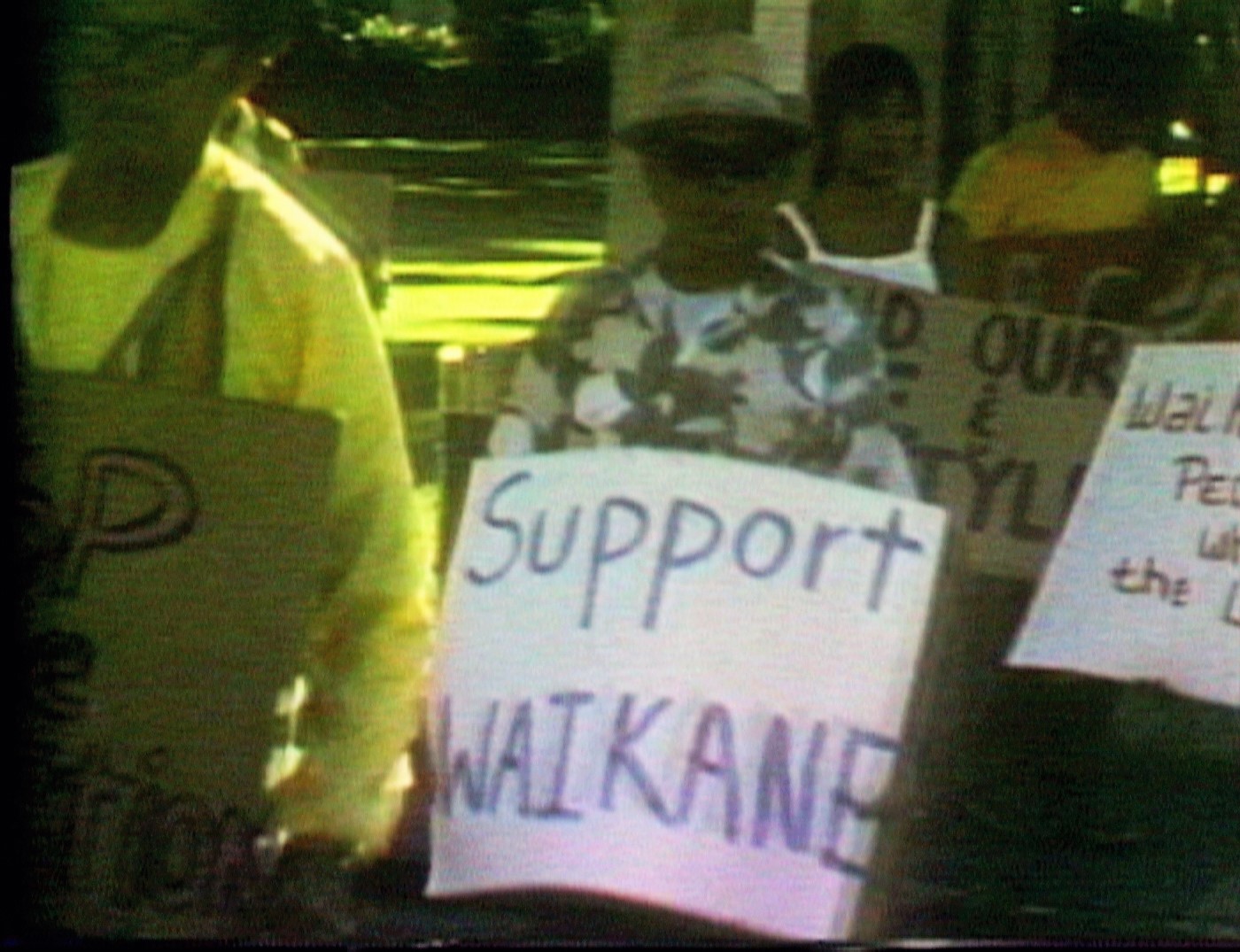 Video frame grab of protester carrying sign saying Support Waikane