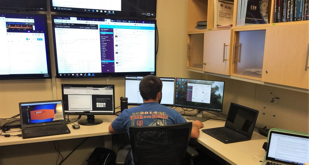 Photo of student at desk with several computer monitors