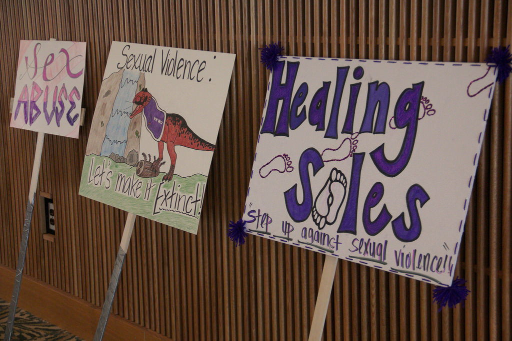 Three signs resting against the wall carrying the Healing Soles message about stepping up against sexual violence