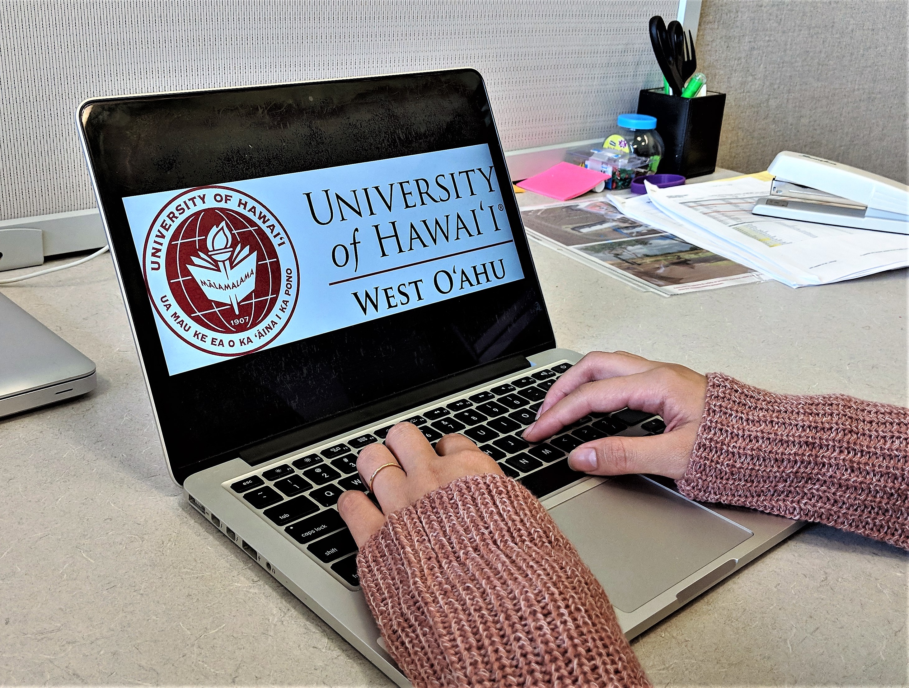 photo of someone's hands typing on a laptop with UHWO logo on the screen