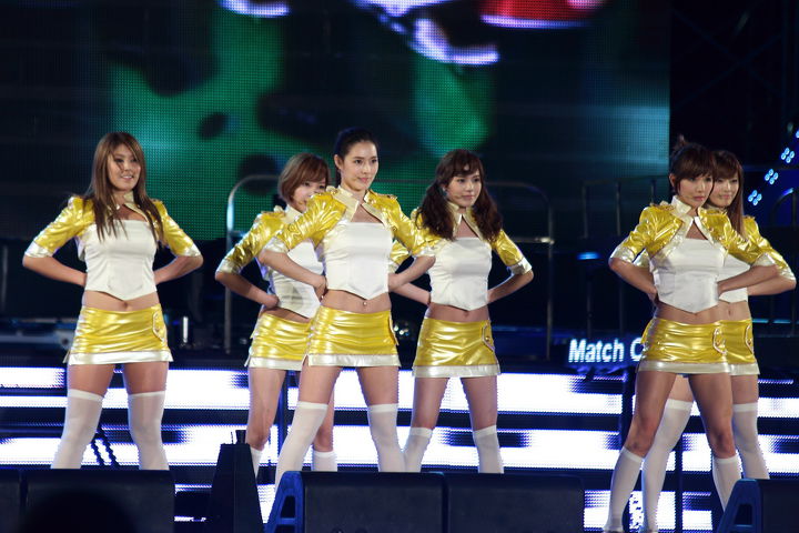 Photo of a K-Pop Girl group performing on stage dressed in yellow and white dresses