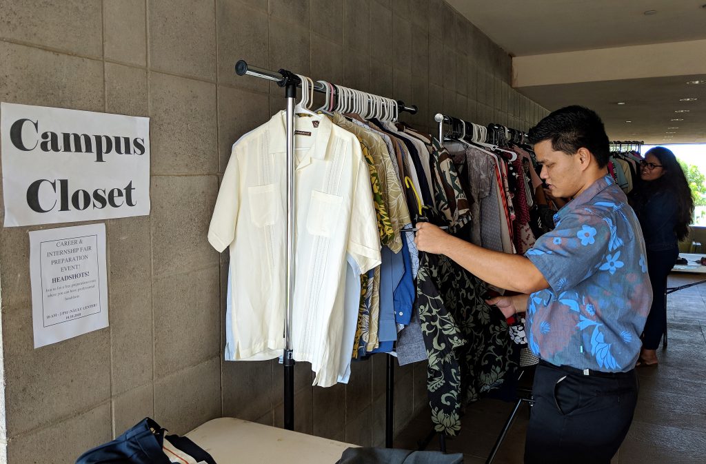 Photo of a wall with Career Closet sign and a student looking at a shirt in front of a rack of shirts