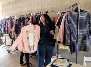 Shot of racks of clothes against a wall and two female students looking at a pink suit