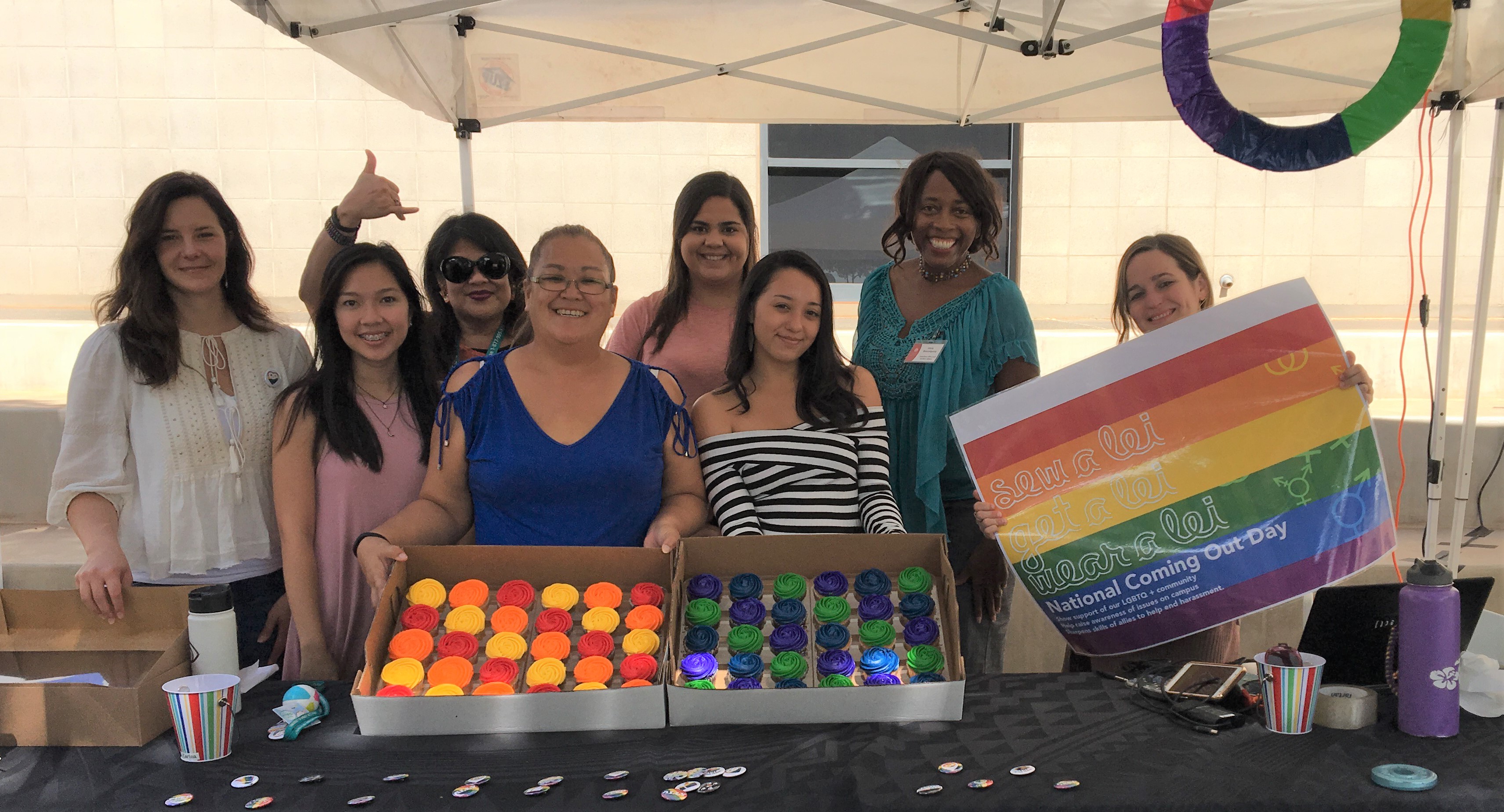 Photo of seven women at a table with multi-colored cupcakes and buttons