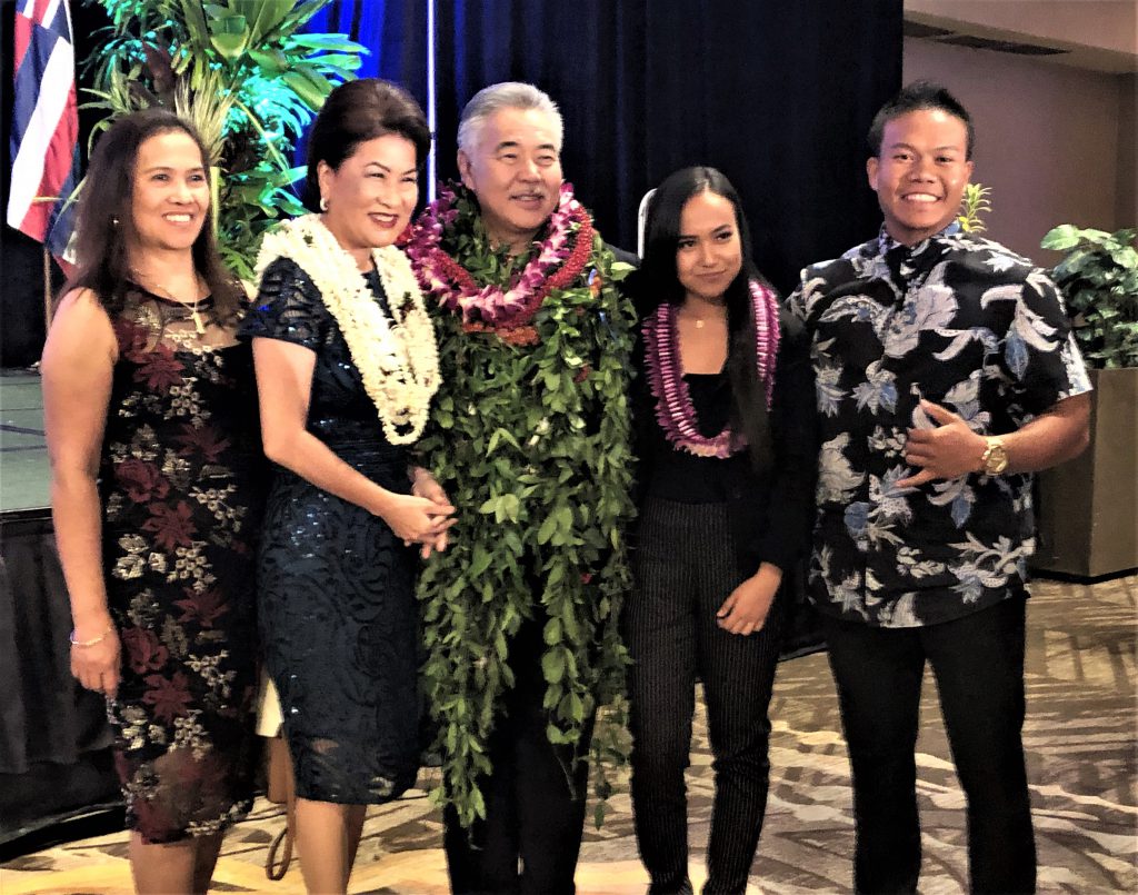 photo of five people standing for a photo. Three of them (Dawn and David Ige and Villanueva) are wearing lei.
