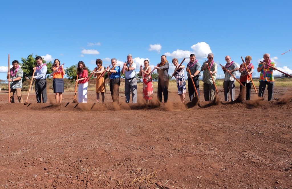 Photo of people in a line, digging in the ground with koa sticks