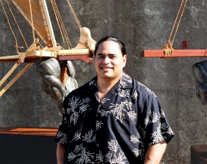 Photo of the artist Kupihea standing in front of two sculptures