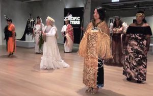 A screen grab from the film Pacific Sisters showing several women dressed in indigenous fashion standing in an art gallery