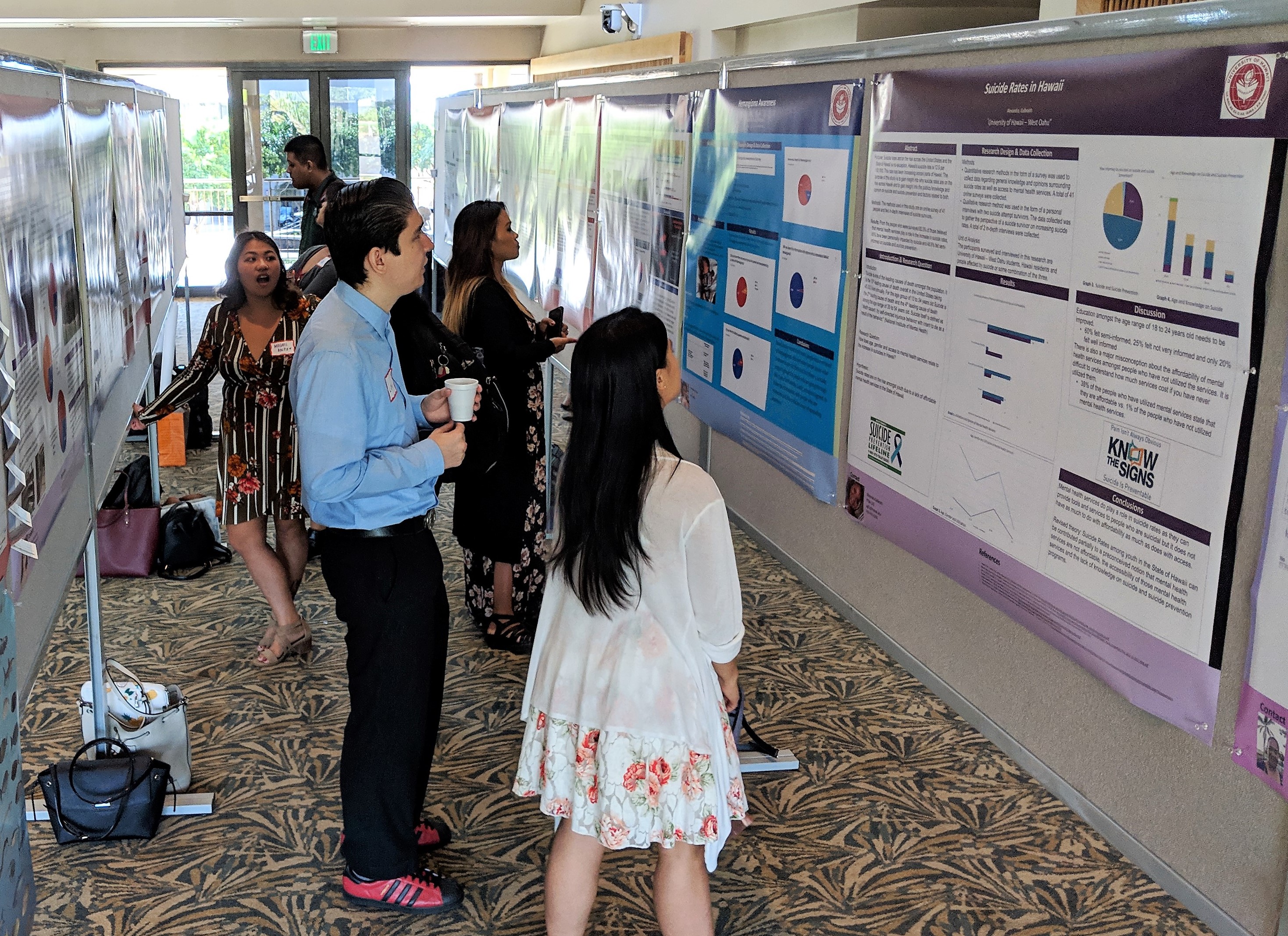 Photo of people looking at research posters that are hung on bulletin boards lined up parallel to each other.