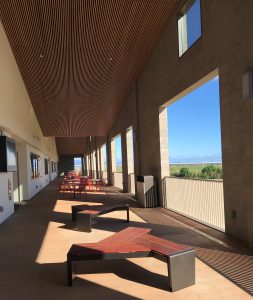 Photo of a broad lanai with openings letting lots of light in. There are seating areas in the middle and classrooms to the left