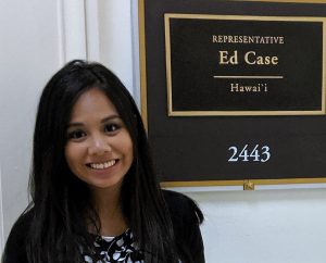 photo of a woman standing next to a sign that says Representative Ed Case Hawaii. She is smiling as she looks into the camera