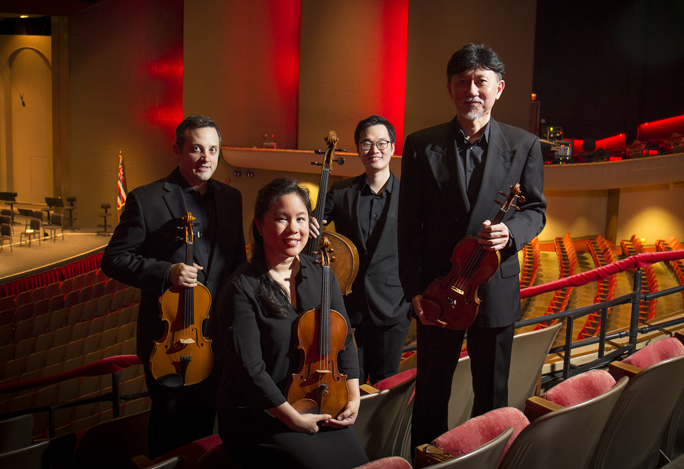 Members of the Chamber Music Hawaii's Galliard String Quartet posing in the audience seating with the stage behind them.