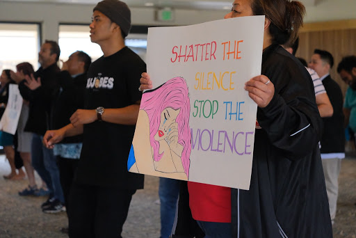 A person holding a poster that says, "Shatter the Silence, Stop the Violence."