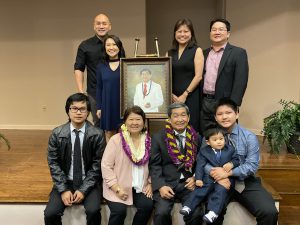 Group photo of Michael Nakasone with his family, all surrounding an easel with a painting of Nakasone.