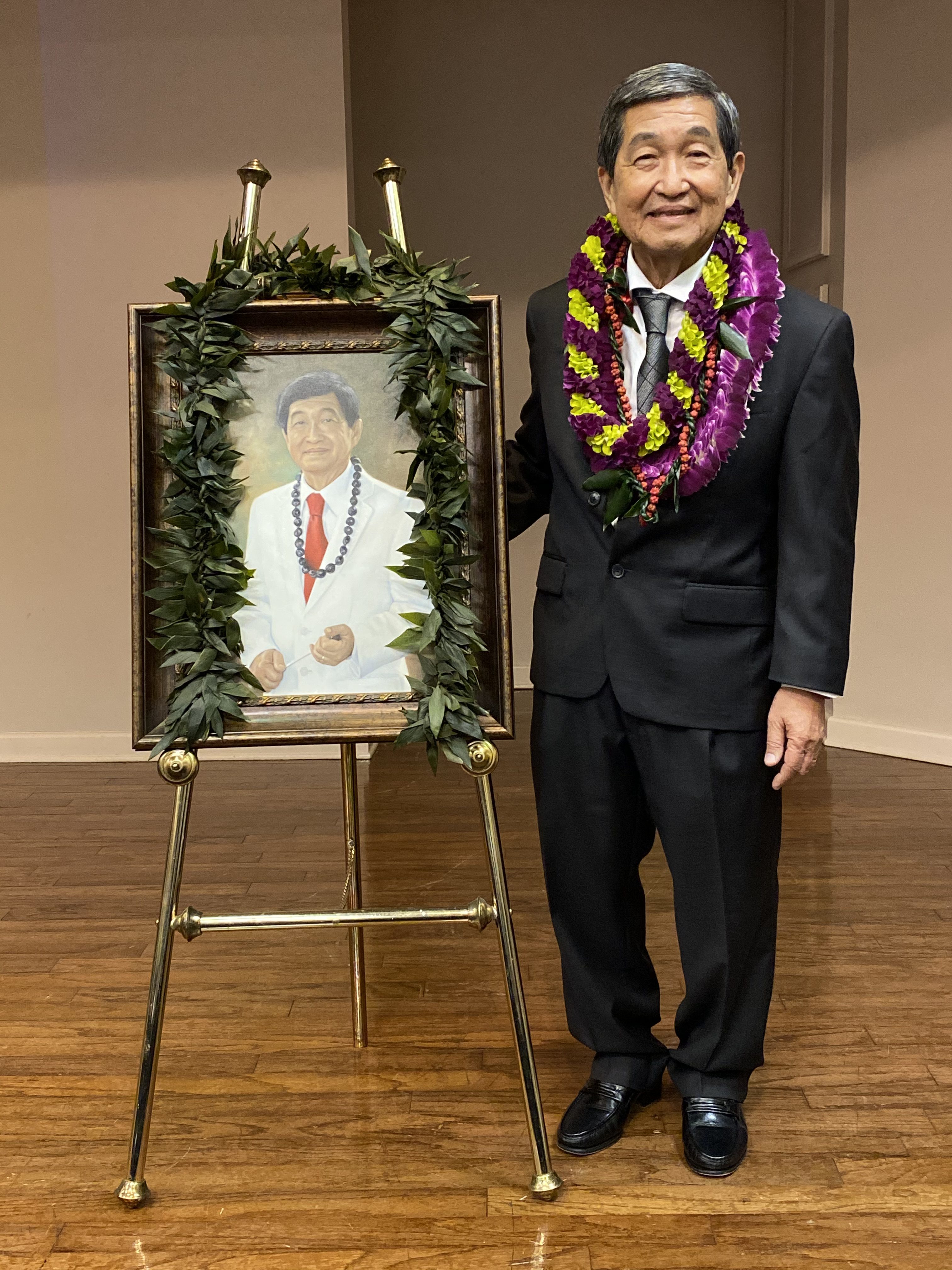 Michael Nakasone standing next to an easel with a painted portrait of himself.
