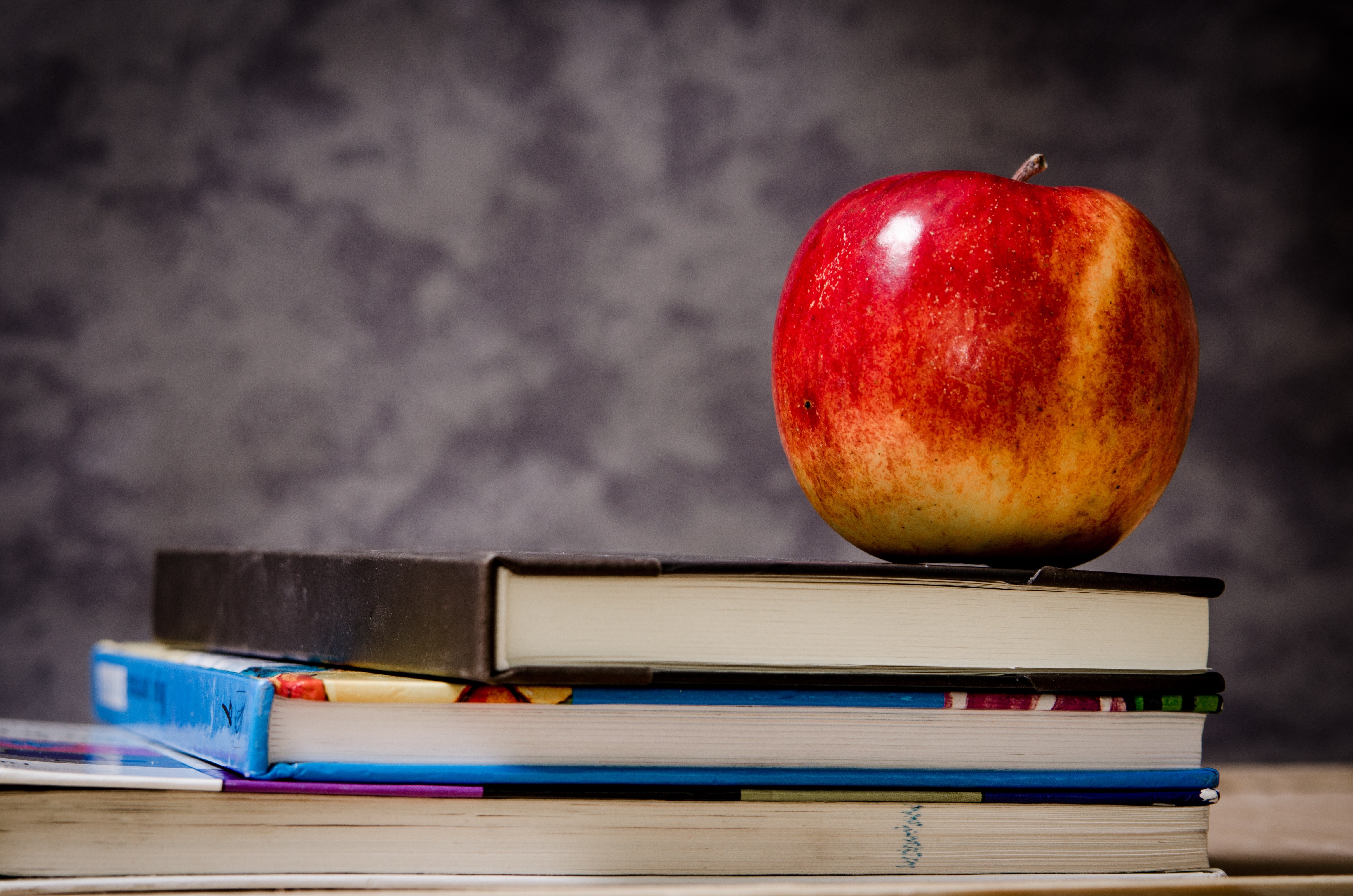 A stack of books with a red apple on top.