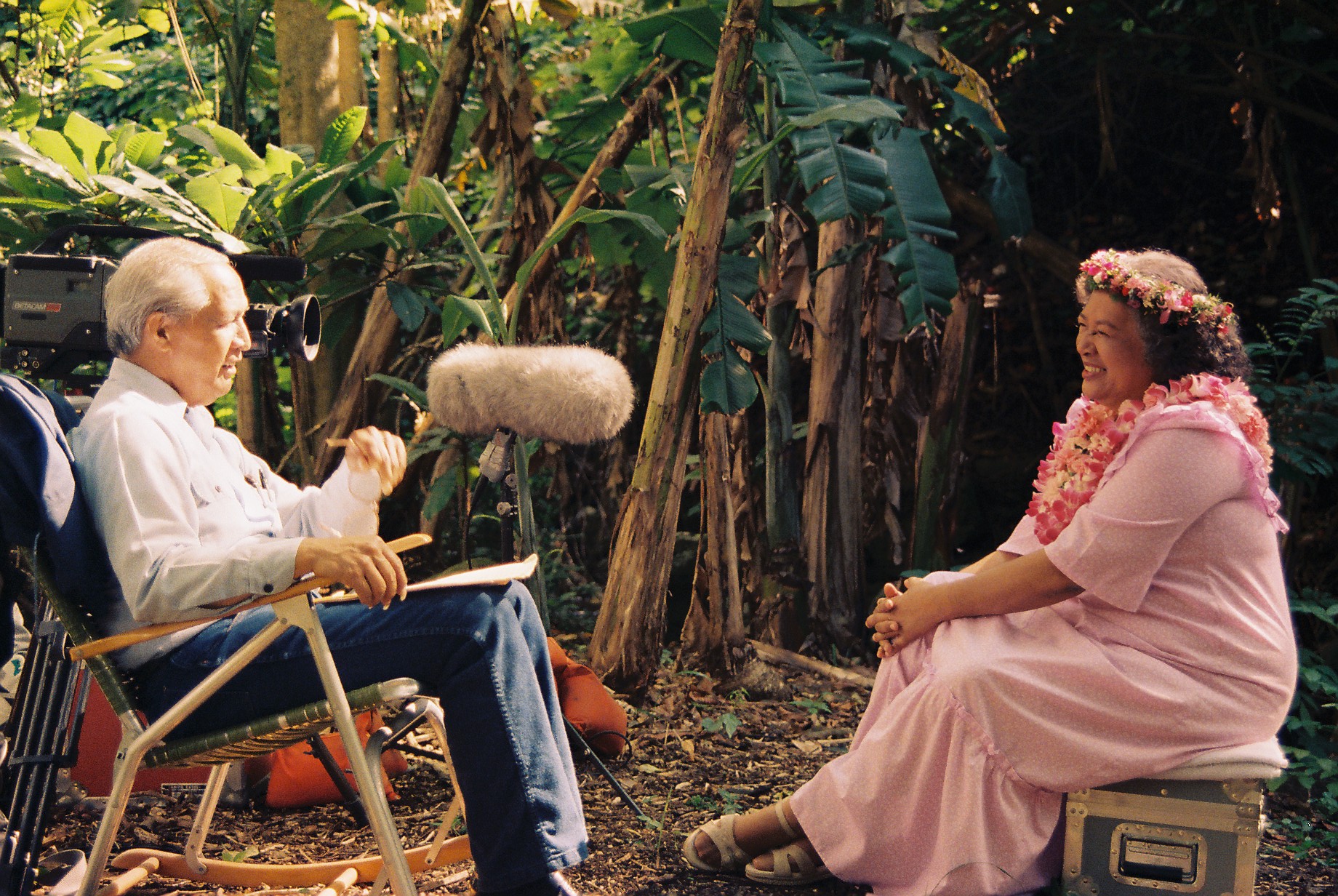 A man interviewing a woman. They are sitting outdoors.