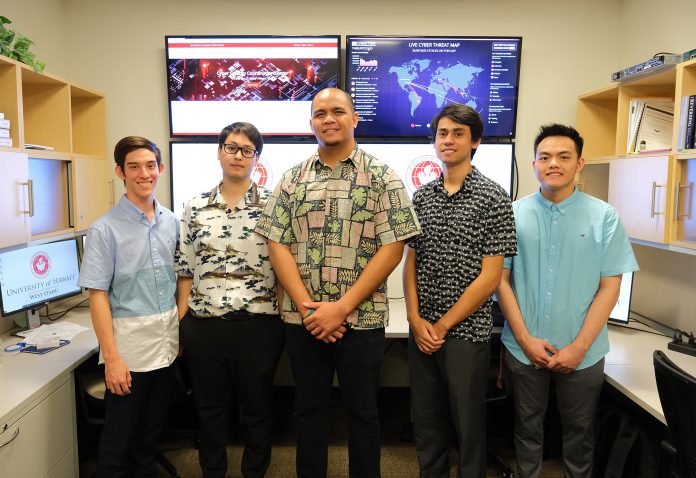 A group of five students standing in front of four wall-mounted monitors at the Cyber Security Coordination Center.