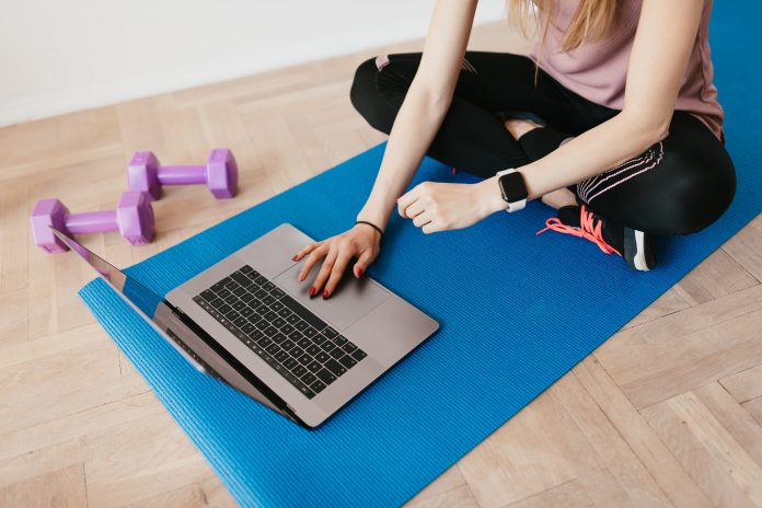 Person on an exercise mat with weights and a laptop.