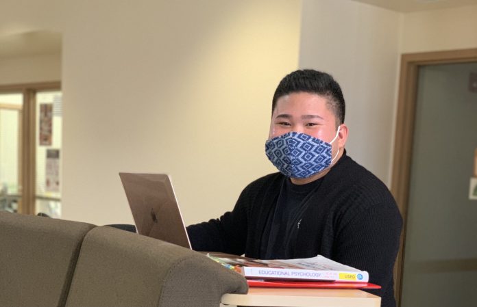 Student wearing a face mask and sitting in front of a laptop.