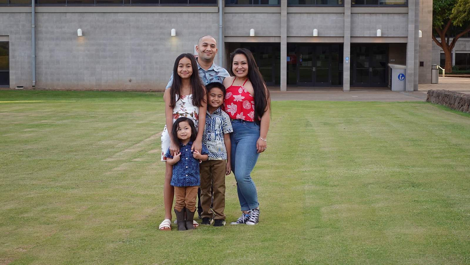 Family posing for a group photo in front of the library at UH West Oʻahu.