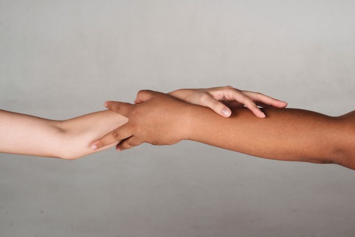 Two arms of different skin colors grabbing hold of each other.