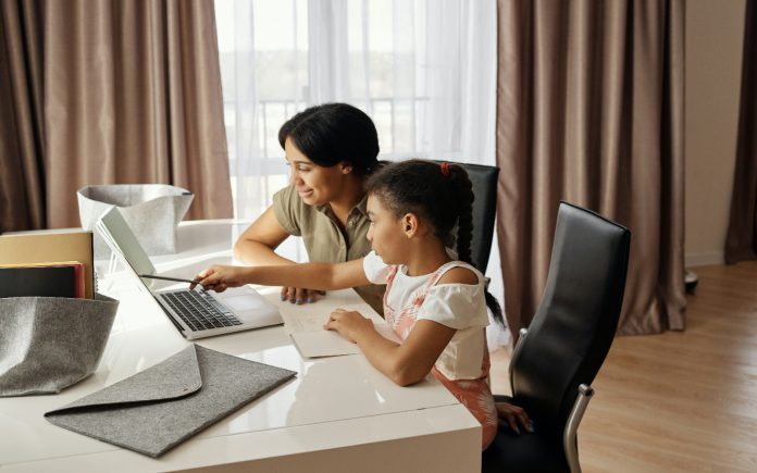 A woman and child sitting at a table and looking at a laptop together.