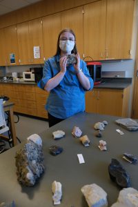 A woman holding a rock with more rock samples on a table in the foreground.