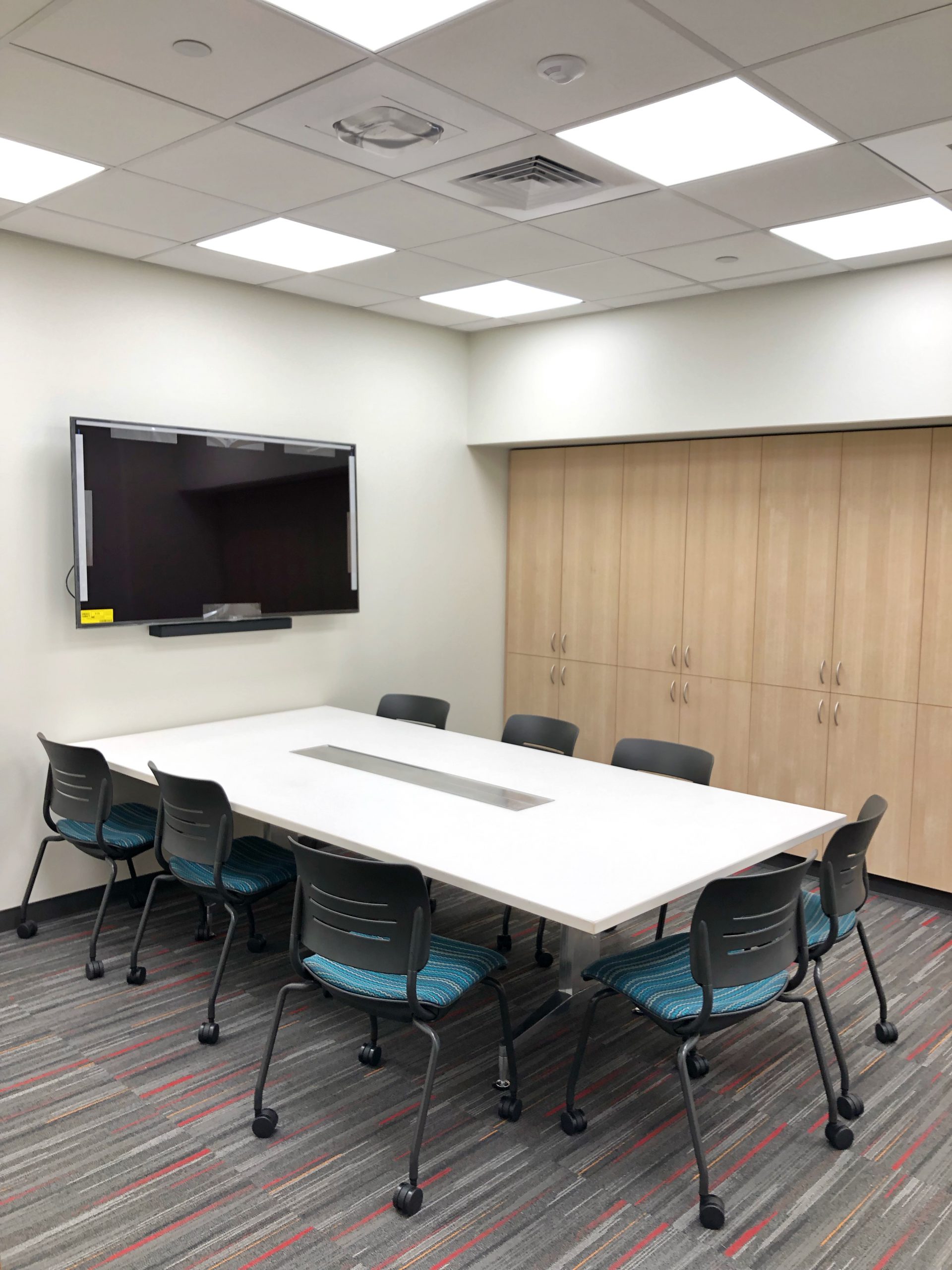 A room with a conference table, chairs, and a wall-mounted screen.