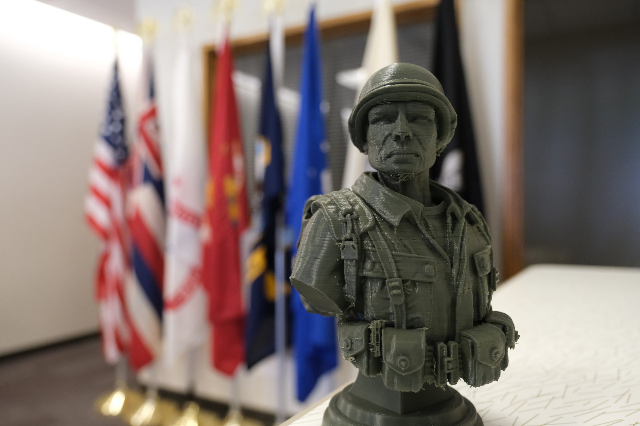 A green bust of an Army soldier with military flags in the background at the UH West Oahu Veterans Center of Excellence