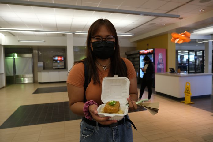 A student holding a takeout container of tofu katsu curry.
