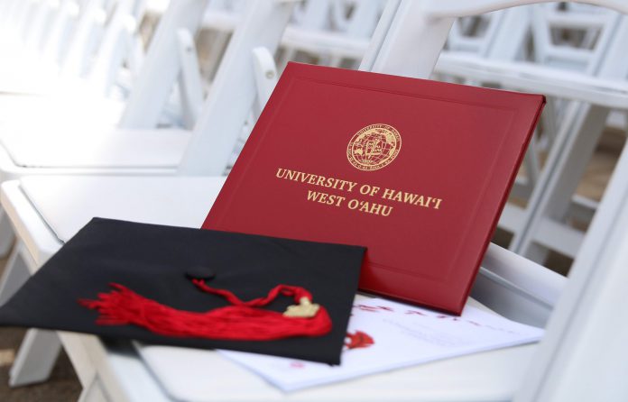 A graduation cap with tassel and a U H West Oahu diploma cover displayed on a white chair.