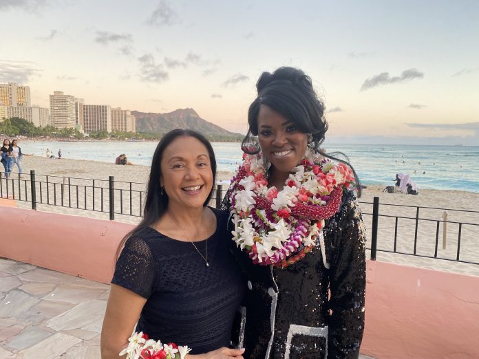 Two women dressed in formal attire in front of the beach.
