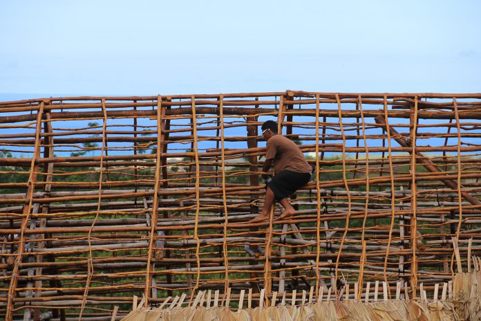A person on top of the wooden frame of a hale in the Waianae Valley.