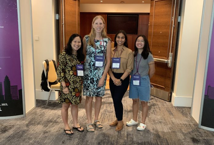 A group of four women smiling and standing outside of a conference room.