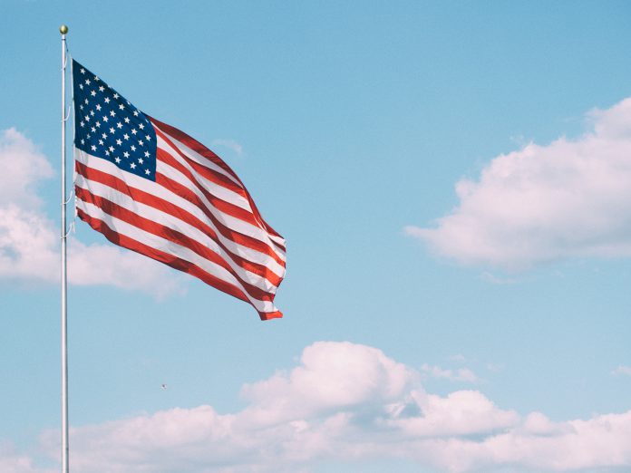American flag flying with the sky and clouds in the background.