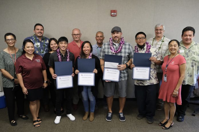 Four students wearing lei and holding certificates, and surrounded by a group of people.