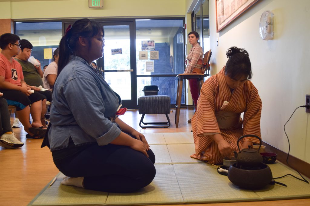 Two women on a floor mat and participating in a Japanese tea ceremony.