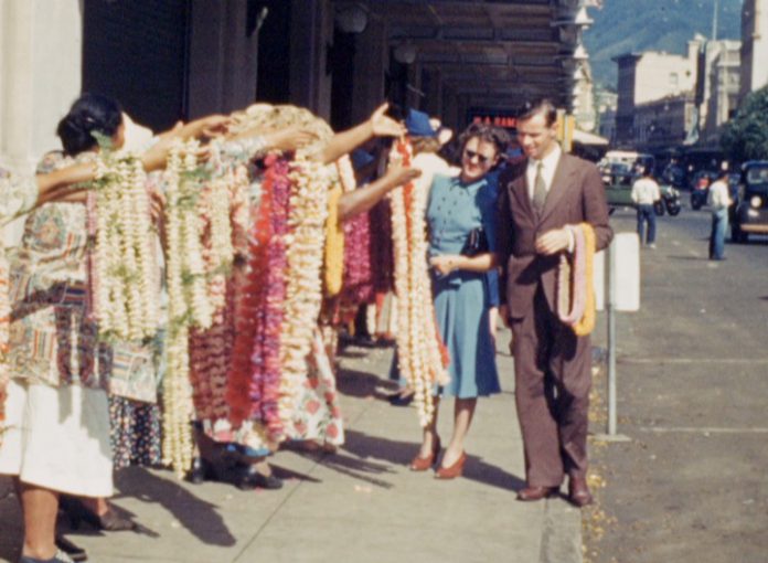 Screenshot of tourists looking at lei on a sidewalk.