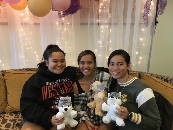 Three students smiling while sitting on a sofa and holding stuffed animals.