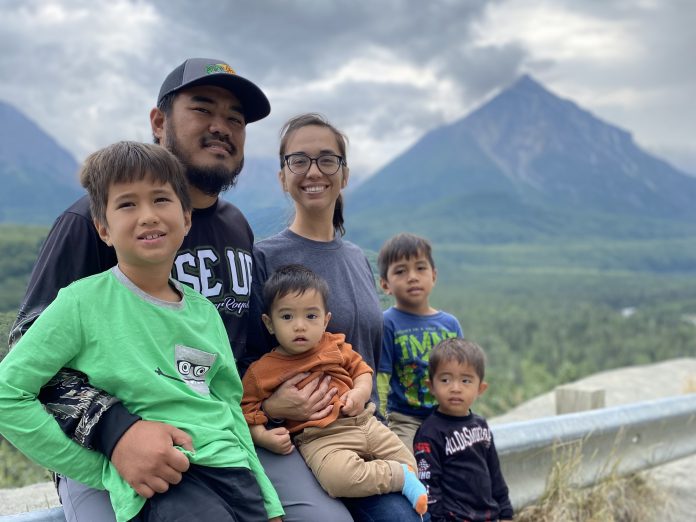 A husband, wife, and four sons posing for a photo outdoors with mountains in the background.
