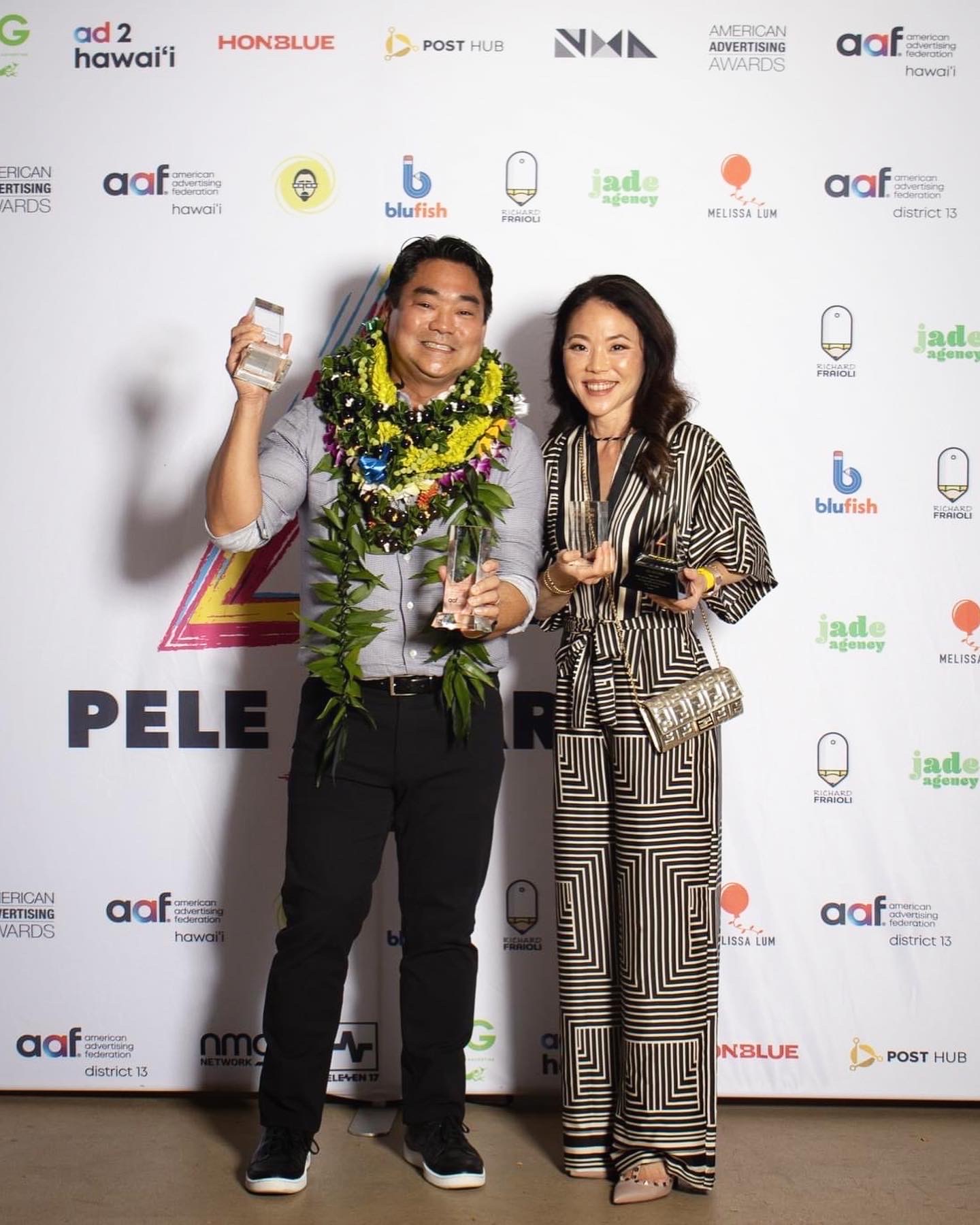 A man holding a trophy next to a woman and both are smiling in front of a backdrop with various logos.