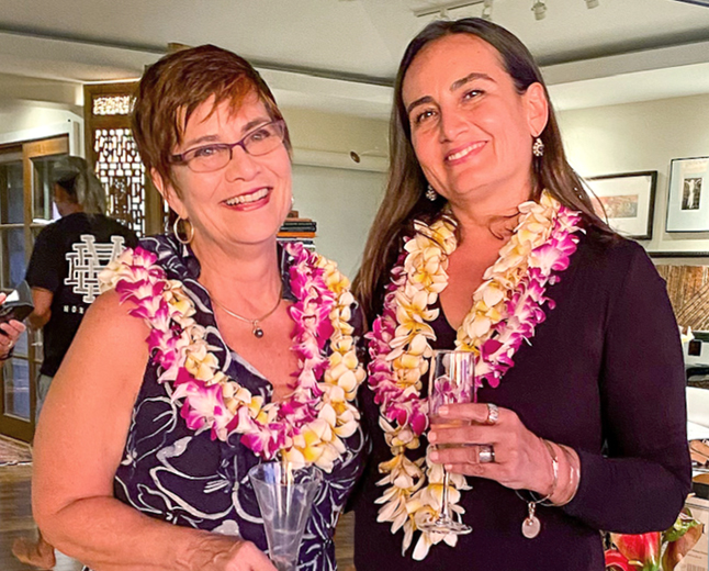 Two women wearing lei and holding wine glasses.