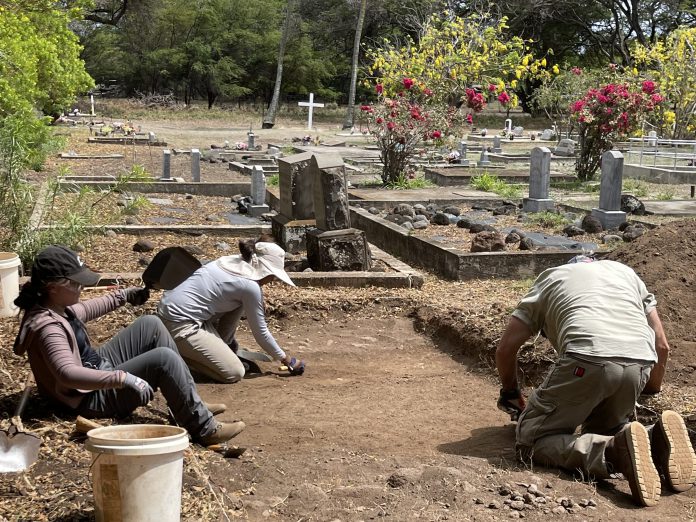 Three people working outdoors at a cemetery.