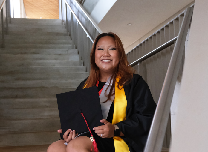 Woman sitting on stairs with her graduation cap and gown.