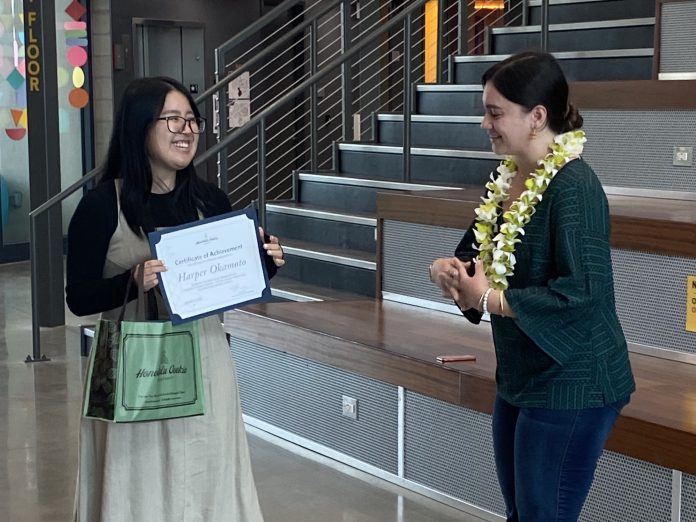 Two women, one holding a certificate and another wearing a lei.