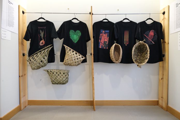 A display of T-shirts and woven baskets hanging on a wall.